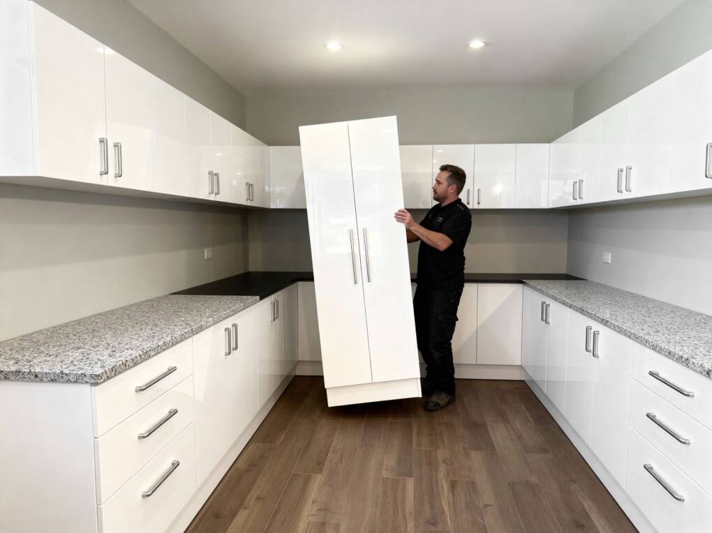 Installer fitting pre-assembled white gloss kitchen cabinets with granite benchtops in a modern Perth kitchen showroom