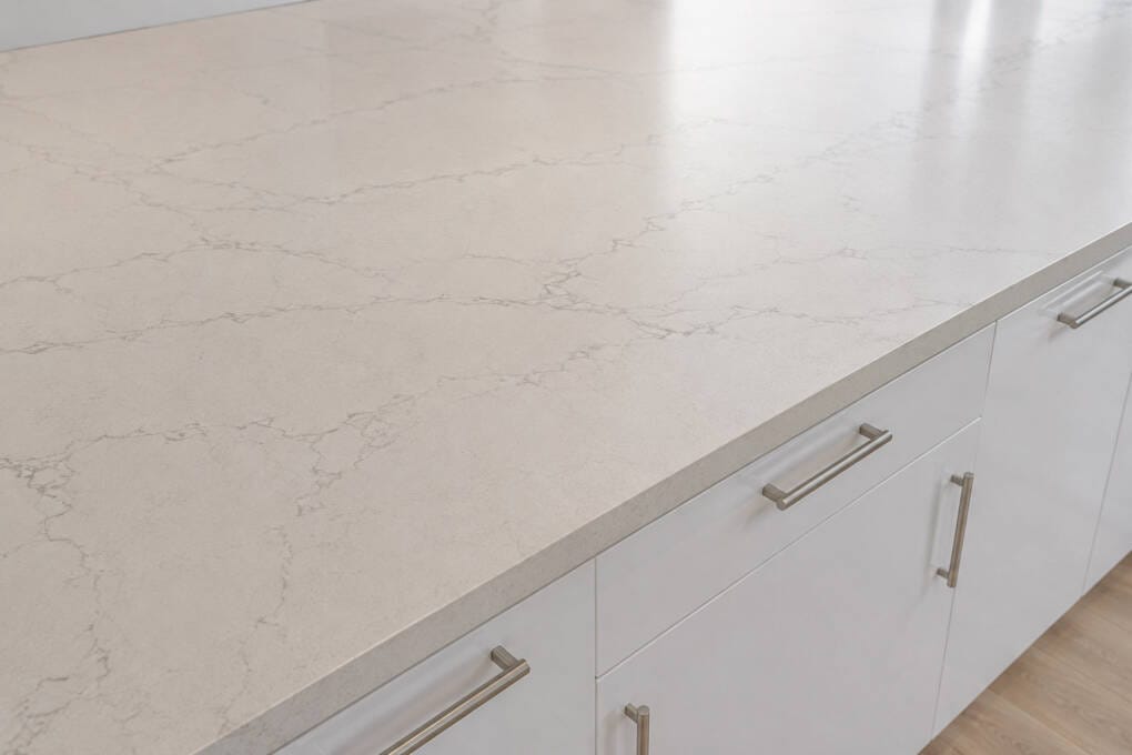 A light, stone-look kitchen benchtop above high-gloss white cabinets with black bar handles.
