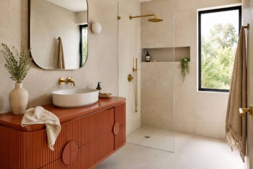 Modern bathroom with a terracotta fluted vanity, warm neutral wall tiles, brass tapware and natural light