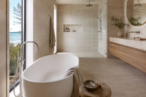 Coastal Australian bathroom with travertine-look tiles, freestanding bath, timber vanity and brushed nickel fittings