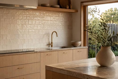 Warm white zellige kitchen splashback with handmade tile texture, timber cabinetry and brass tapware