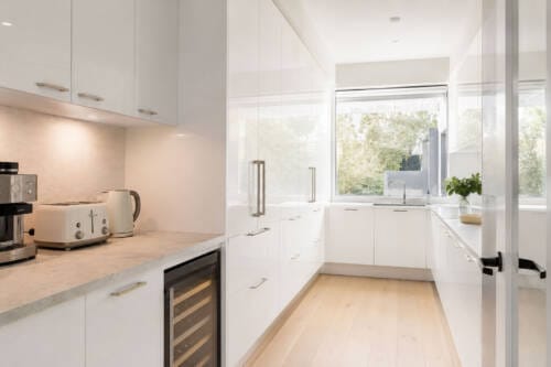 White high-gloss butler's pantry with plain-profile cabinetry, secondary sink and appliance bench