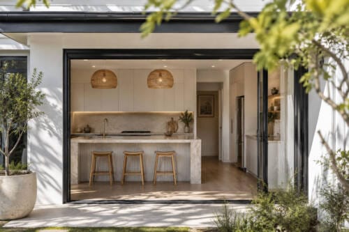 Exterior view into a modern Australian kitchen with large black-framed glass doors and alfresco connection