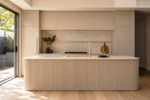 Warm neutral kitchen with a fluted island front, brass tapware and natural stone benchtop