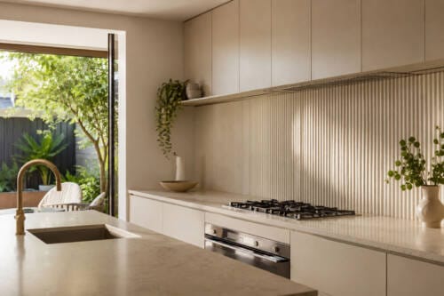 Warm neutral kitchen with a fluted ceramic splashback, smooth cabinetry and brass tapware