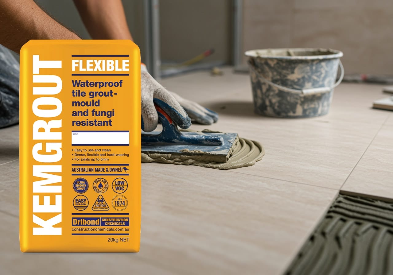 Professional tiler applying Kemgrout flexible waterproof tile grout to beige floor tiles, using a trowel for even application