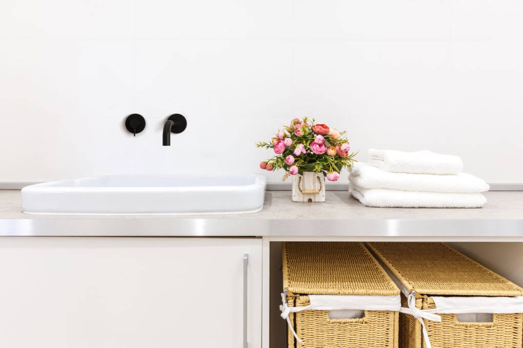 Modern laundry with matte black wall tapware above utility sink, styled with fresh towels and flowers