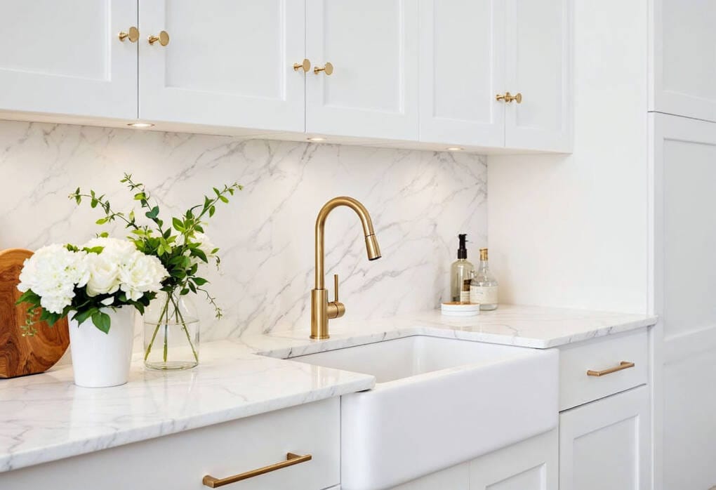 Modern kitchen with white cabinets, veined stone benchtop and splashback, brushed brass tapware, and Hamptons-inspired styling