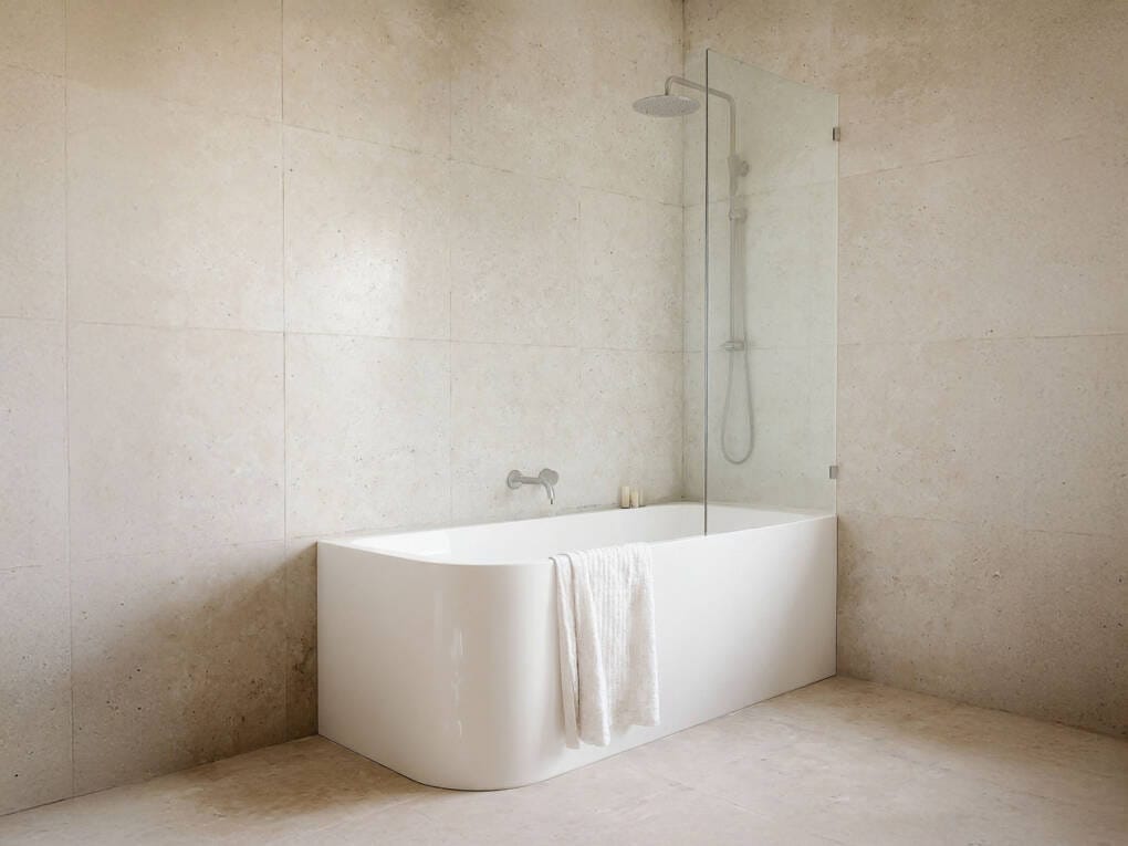 corner bath with shower screen in modern beige tiled bathroom