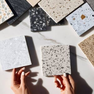 hands holding terrazzo tile samples with natural and porcelain look terrazzo tiles on marble surface