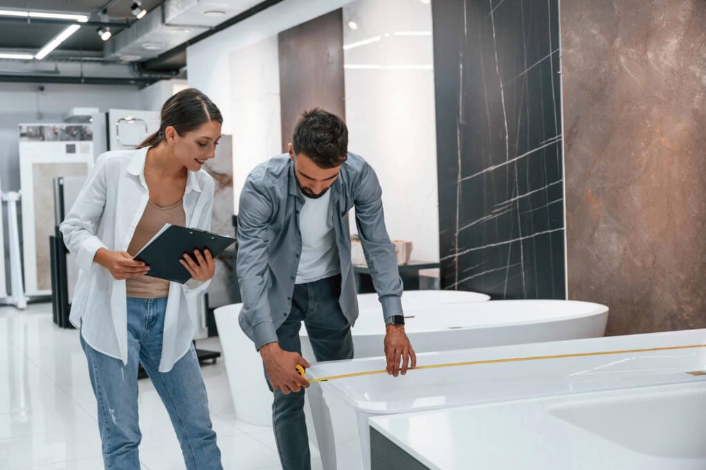 Couple measuring a bath in Perth bathroom store, comparing styles and finishes before choosing the right products for renovation