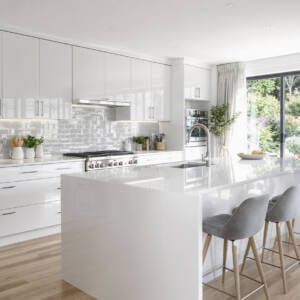 Modern white kitchen featuring gloss cabinets, sleek cupboards, and a large island bench with bar stools, showcasing contemporary Perth kitchen design