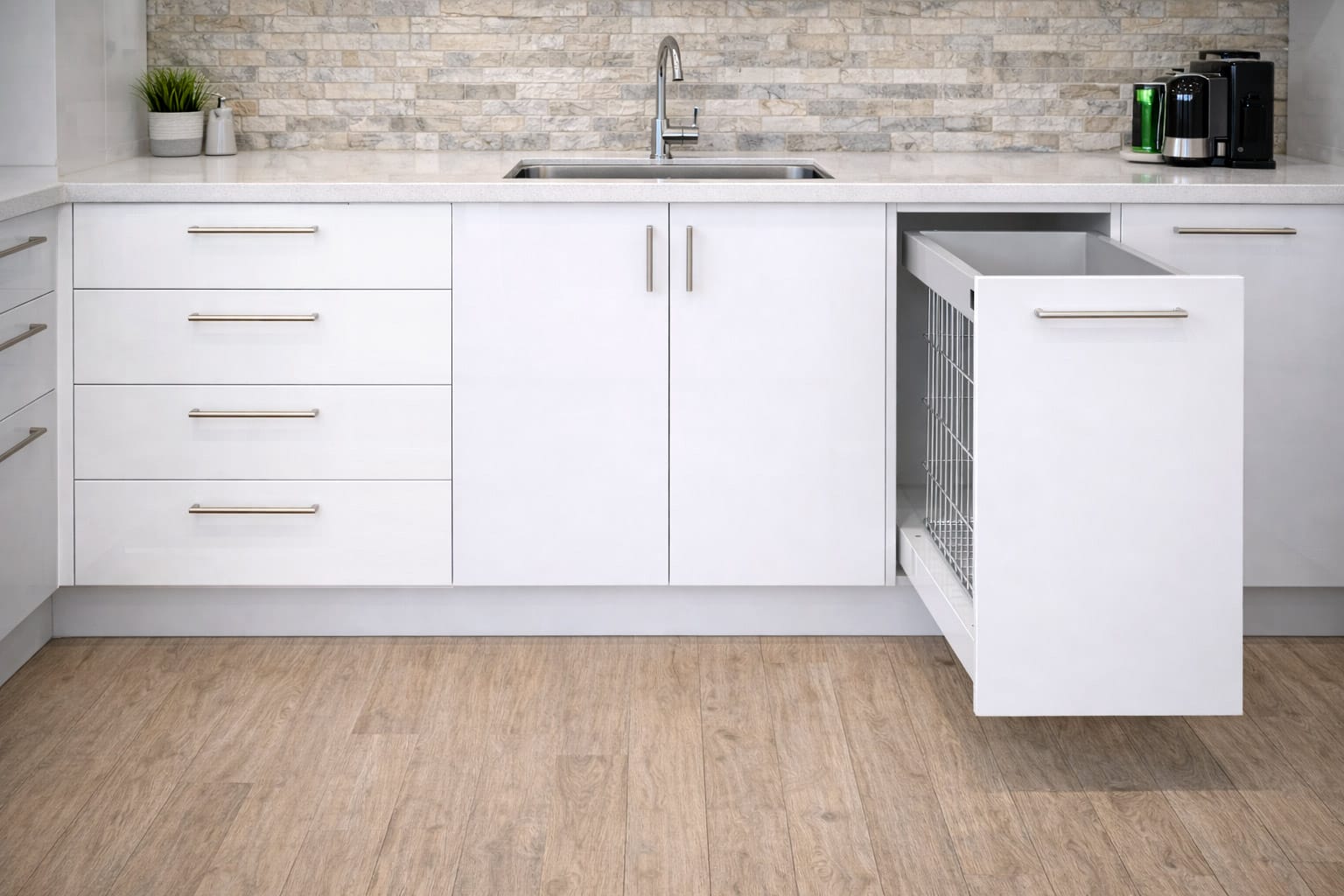 White kitchen base cabinets with integrated drawers, sink unit, and pull-out wire basket, set beneath a stone benchtop and tiled splashback.