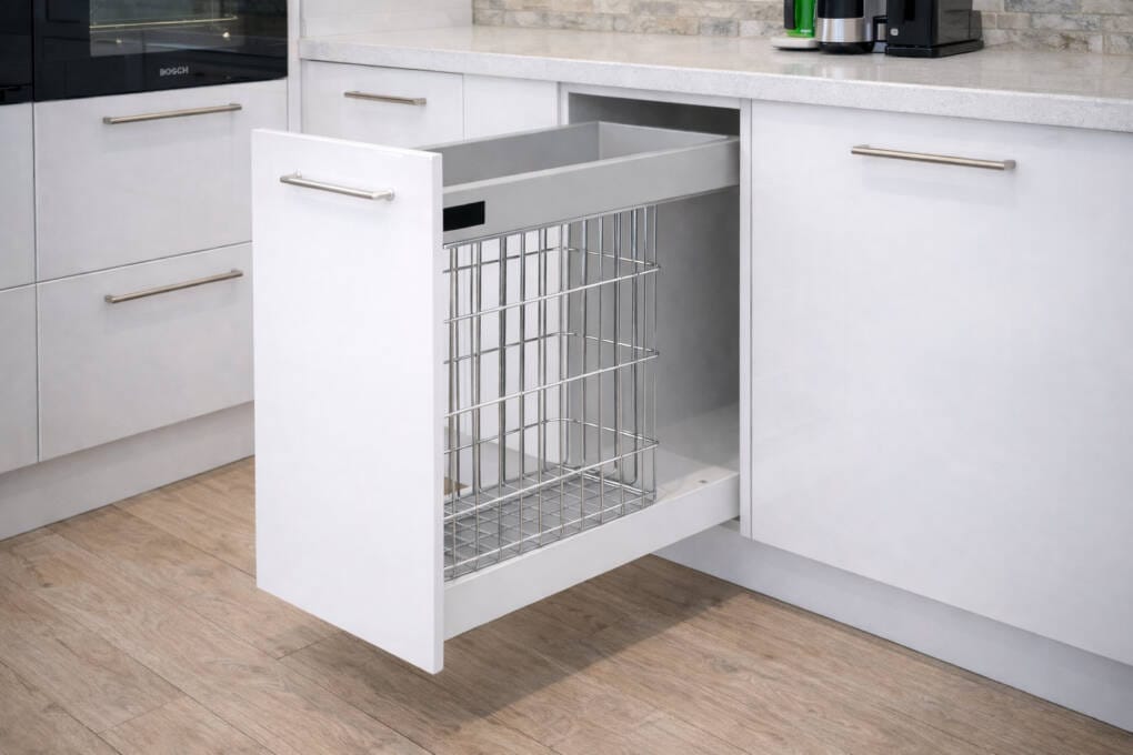 White kitchen base cabinet with pull-out wire basket drawer, stone benchtop above, and integrated handle in a modern kitchen setting.