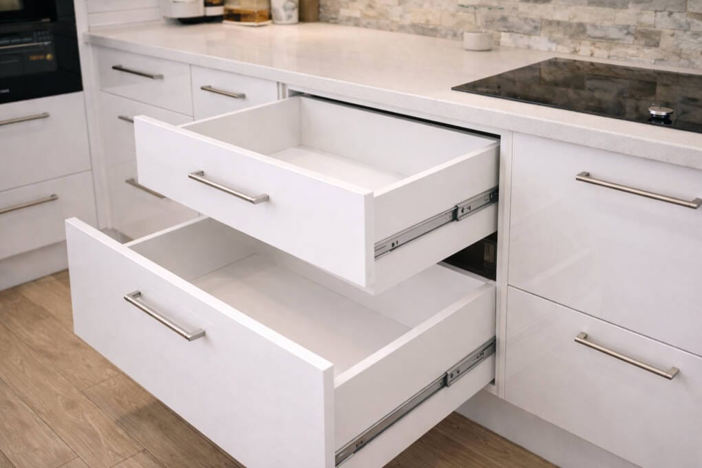 White kitchen base cabinets with soft-close drawers extended, featuring stone benchtop and modern stainless steel handles.