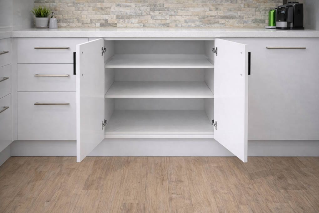 White double door base cabinet with doors open, showing adjustable internal shelving beneath a stone benchtop in a modern kitchen.