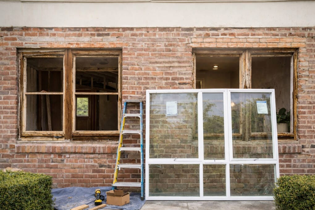Older brick home with removed timber windows beside new replacement window showing size mismatch during renovation