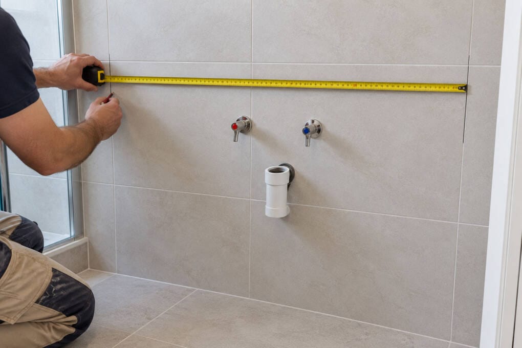 Tape measure across a bathroom wall marking vanity width around the waste and water points