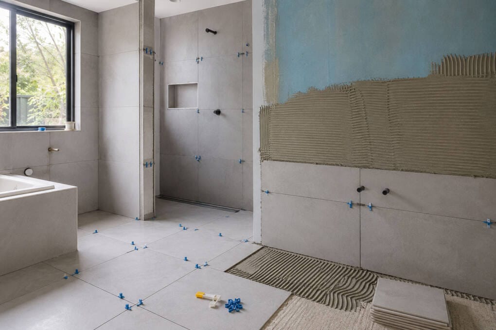 Bathroom mid-renovation with wall and floor tiles being installed, waterproofing prep and tile levelling clips
