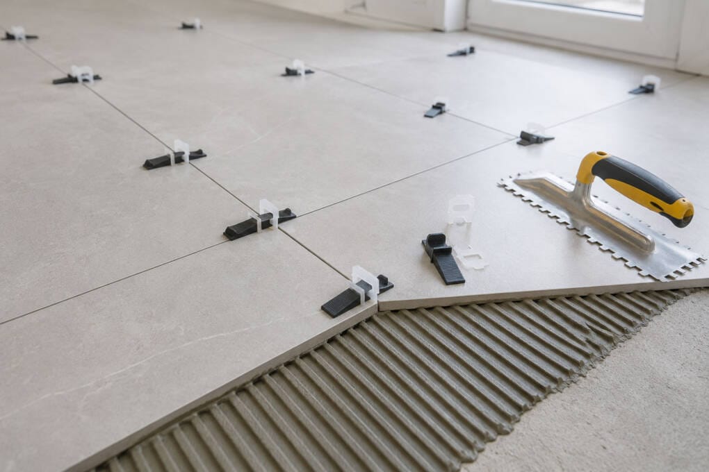 Close-up of large-format floor tiles being installed with levelling clips, wedges, spacers, adhesive and trowel