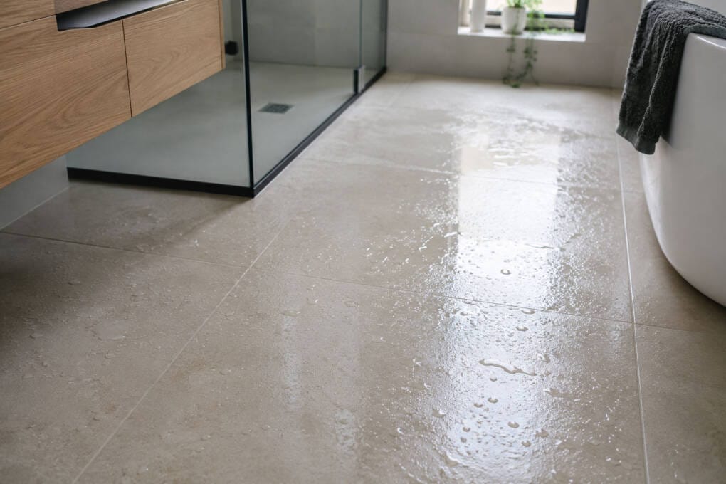 Close-up of glossy bathroom floor tiles with water droplets showing why slip rating and tile finish matter