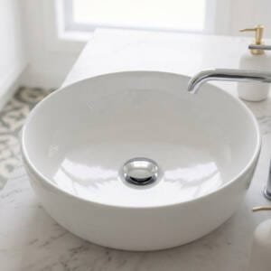 A modern chrome pop-up waste installed in a white ceramic bathroom basin next to a matching basin mixer tap